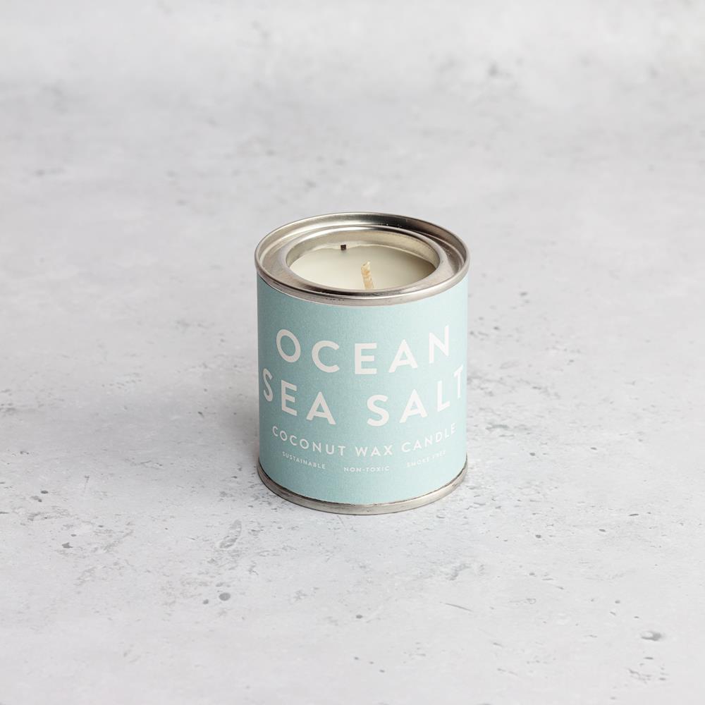 A light blue tin labelled Ocean Sea Salt coconut wax candle sits on a light grey, textured surface with its lid removed.