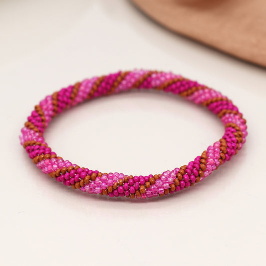 A twist bead bracelet, featuring bright pink and brown beads arranged in a spiral pattern, rests elegantly on a light-coloured surface.