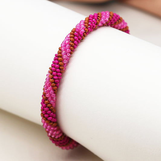 A bright pink and brown twist bead bracelet elegantly rests on a white cylindrical surface, adding a vibrant touch to any outfit.