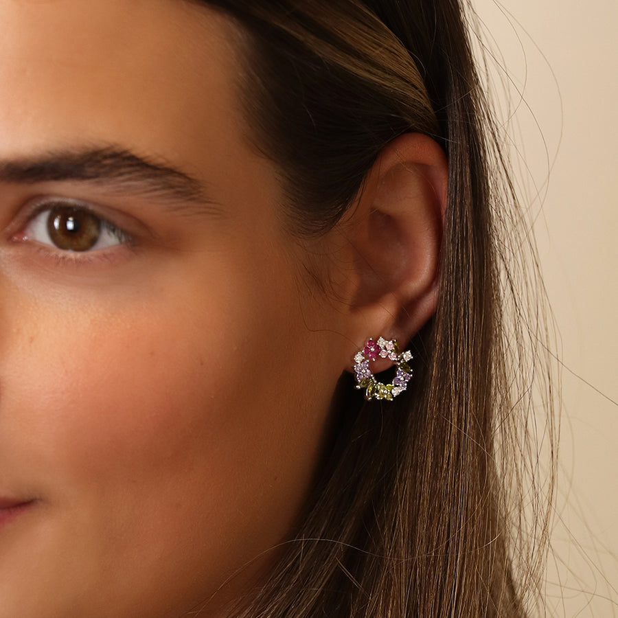 Close-up of a person wearing exquisite floral circle studs adorned with pink and purple faceted crystals, shimmering brilliantly against silver-plated earrings.