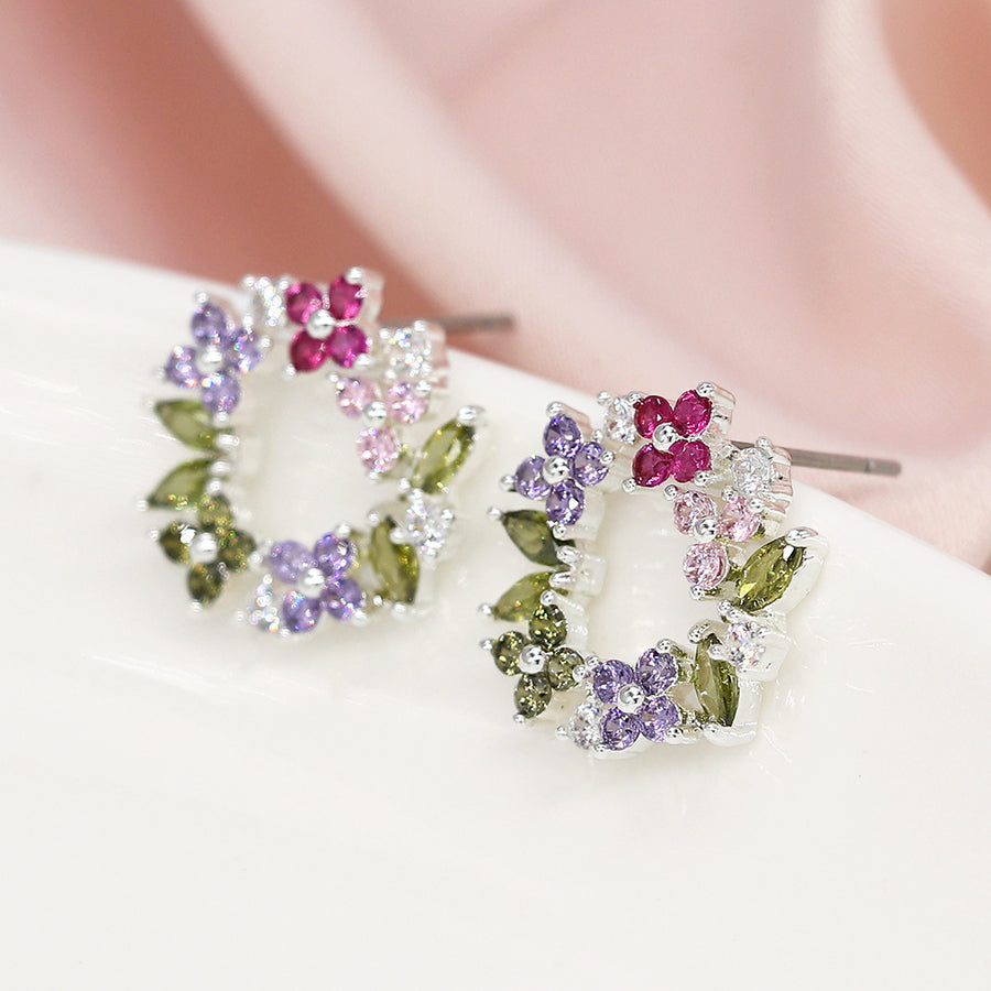 Floral Circle Studs embellished with clusters of pink, purple, and green faceted crystals set in silver, resting beautifully on a soft pink fabric background.