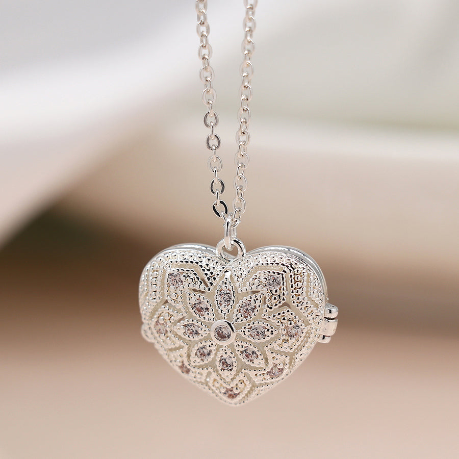 A heart-shaped silver-plated locket with intricate floral engravings hangs from a fine chain, a stunning addition to any jewellery collection.
