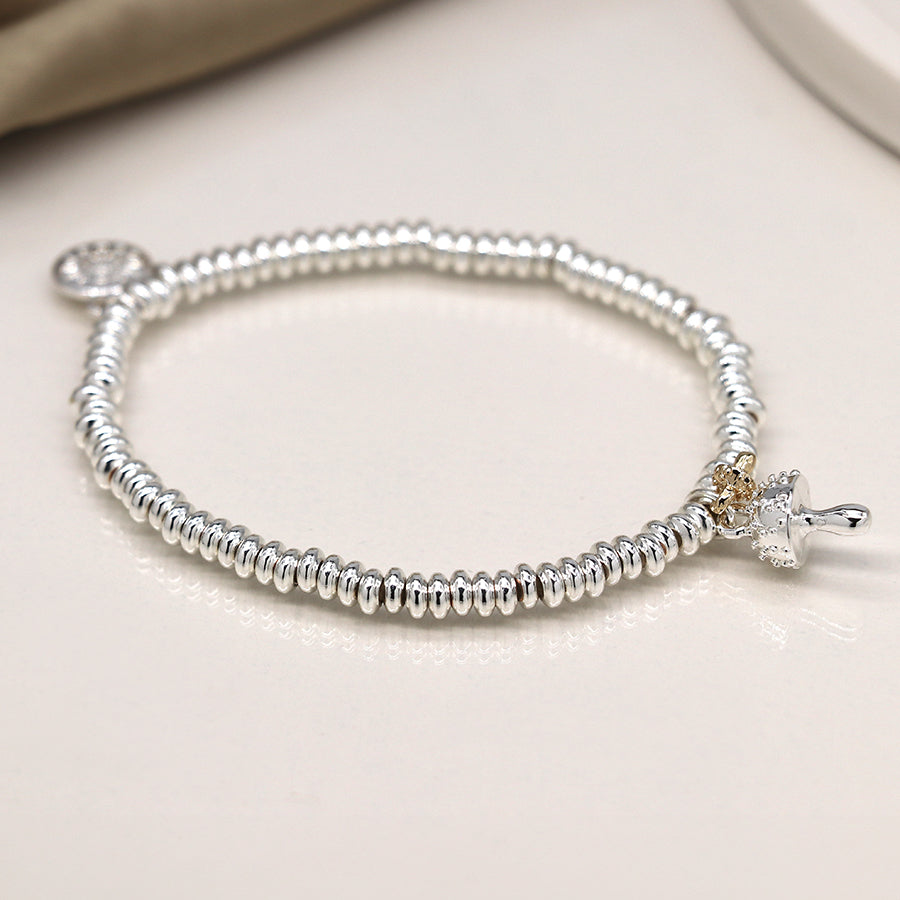 A silver beaded bracelet exudes edgy elegance with its small cross and round pendant charm, resting on a beige surface.