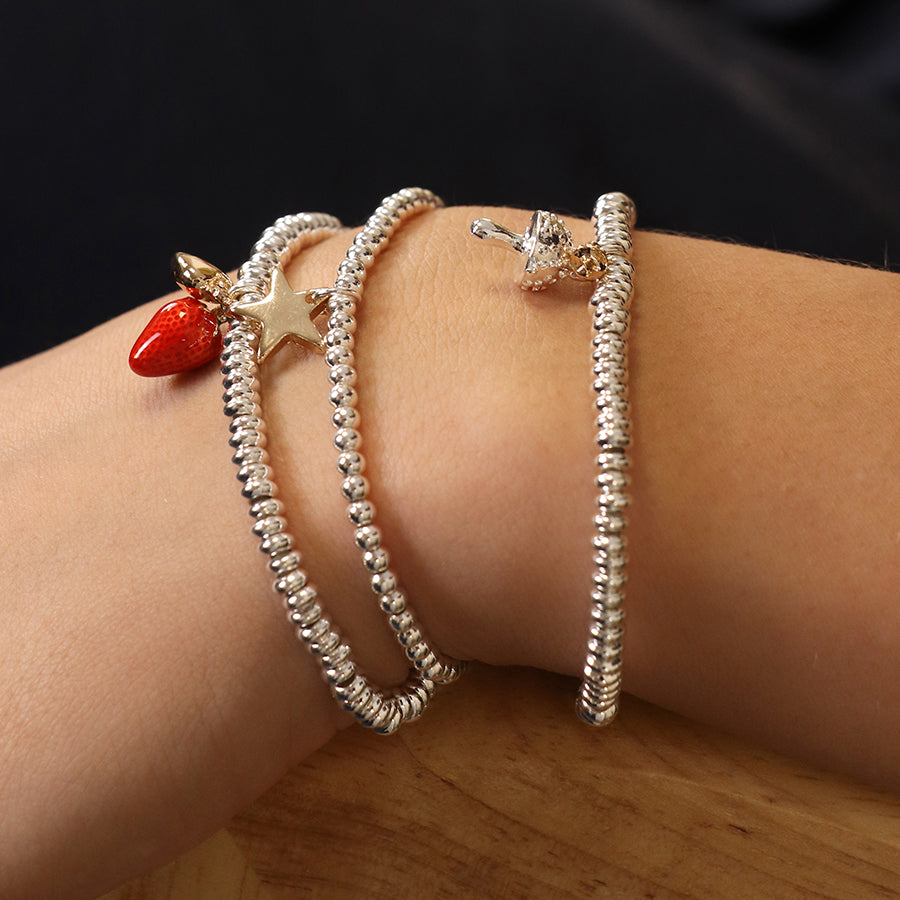 A wrist graced with a chic edginess, this silver-plated charm bracelet features an intricately coiled silver design with a red strawberry, gold star, and a whimsical toadstool charm.
