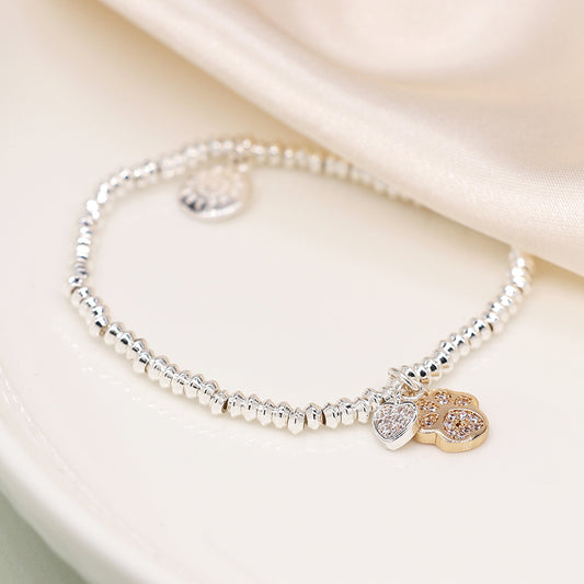 A silver-plated charm bracelet with a golden paw charm embellished with rhinestones, elegantly placed on a pale surface with a soft fabric in the background.