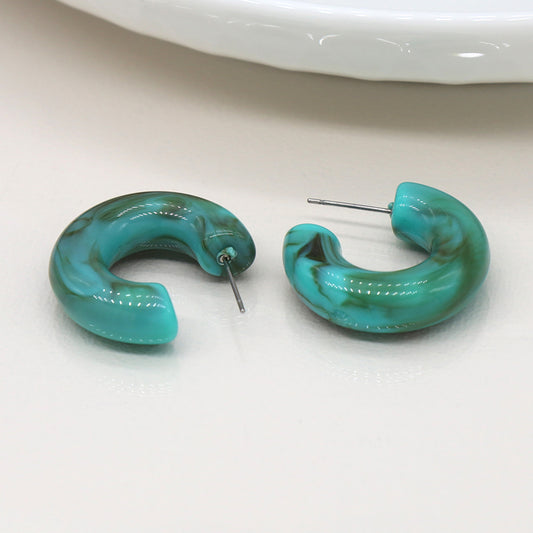 Two jade green, C-hoop stud earrings with a marbled effect are placed on a neutral background.