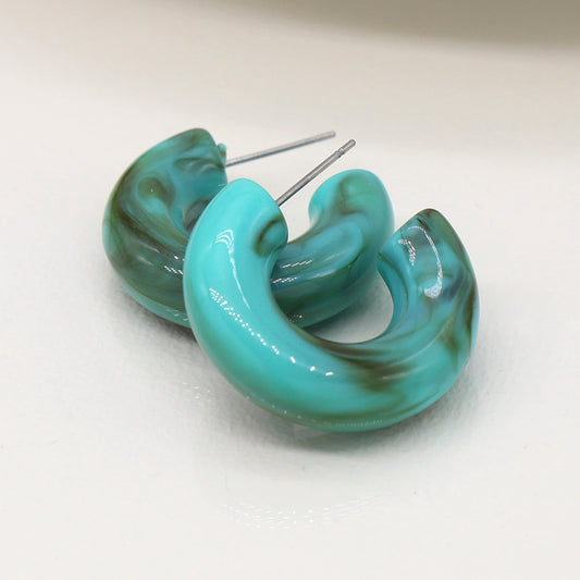 Two turquoise and brown marble design C-hoop stud earrings with metallic posts rest elegantly on a white surface.