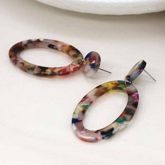 Two unique pieces of dangle earrings feature colourful marbled oval drops with a terrazzo effect, resting on a white surface.