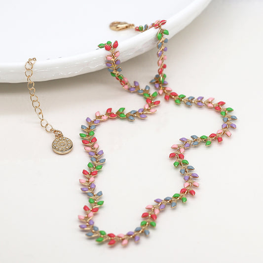 A colourful beaded necklace, featuring small leaf-shaped beads in red, green, purple, and pink on a white surface. This faux gold necklace boasts a gold chain and round charm, making it a sophisticated jewellery statement piece.