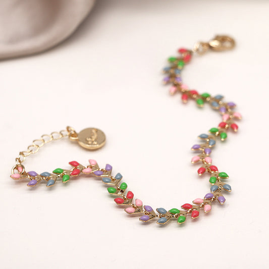 The Golden Pastel Epoxy Droplets Bracelet is a luxurious accessory, featuring a gold chain with colourful leaf-shaped beads in green, blue, pink, and red hues. Its sophisticated design includes an engraved gold charm on a light background.