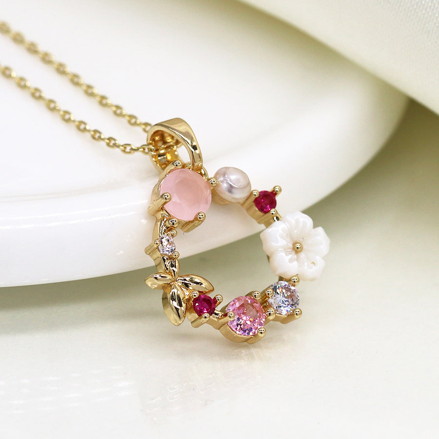 Fake gold-plated necklace featuring a round pendant adorned with pink, white, and clear crystals, a small pearl, shell flowers, and red stones—evoking the appearance of a delicate floral wreath.
