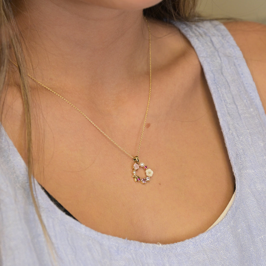 Close-up of a person wearing a faux gold-plated necklace with a circular pendant featuring purple and white gemstones, set against a light blue textured blouse.