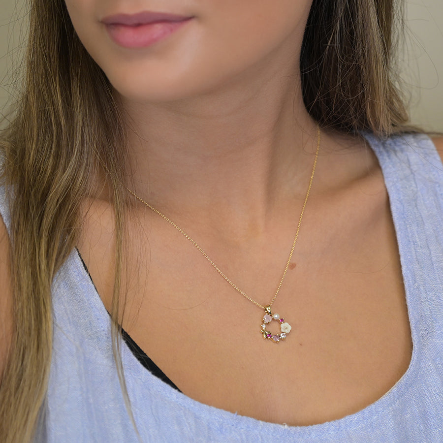 A woman wearing a delicate imitation gold-plated necklace with a small pendant shaped like a crescent moon, adorned with colourful shell flowers.