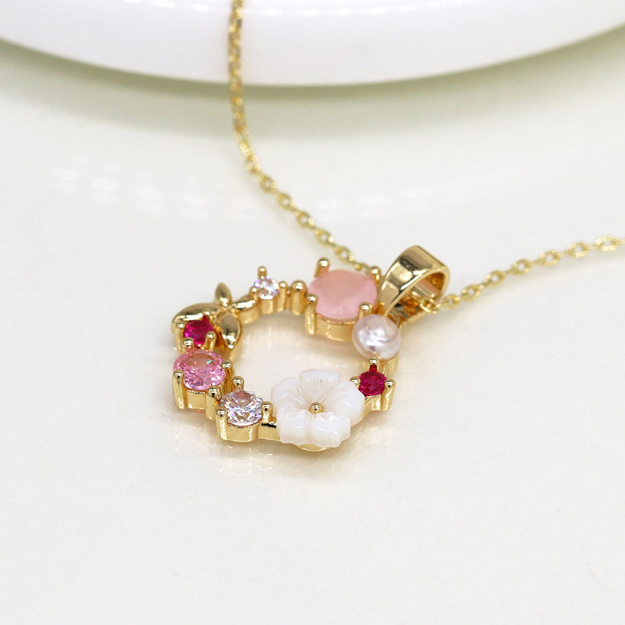 Imitation gold-plated necklace with a heart-shaped pendant adorned with colourful gems and shell flowers, featuring a white flower and pink and red stones.