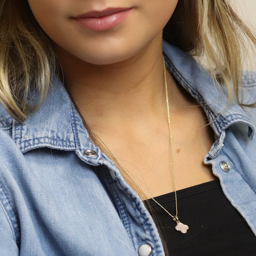 A woman puts on a denim shirt and black top, her look enhanced by a statement piece—a faux gold chain with a delicate pink pendant.