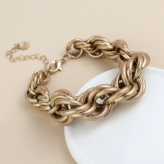 Chunky chain bracelet with interlocking links, lobster clasp, and an adjustable extender—this gold bracelet makes striking statement jewellery, shown on a beige surface with a white circular prop.
