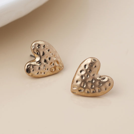 A pair of gold heart earrings with a hammered finish, showcasing a textured, dimpled surface, set against a neutral background.