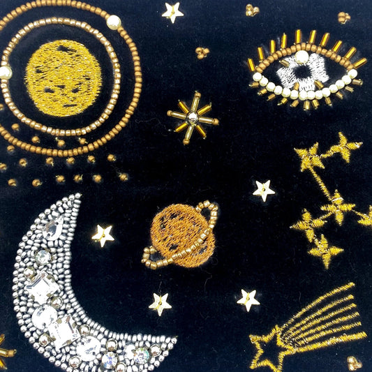 Embroidered and beaded designs featuring a moon, sun, stars, planets, constellations, and an eye decorate this vegan-friendly make-up pouch crafted from black fabric.