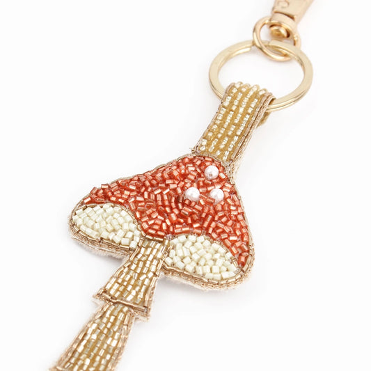 Handcrafted in India, this beaded keyring shaped like a mushroom features red, white, and beige beads with elegant copper accents, all attached to a gold key ring.