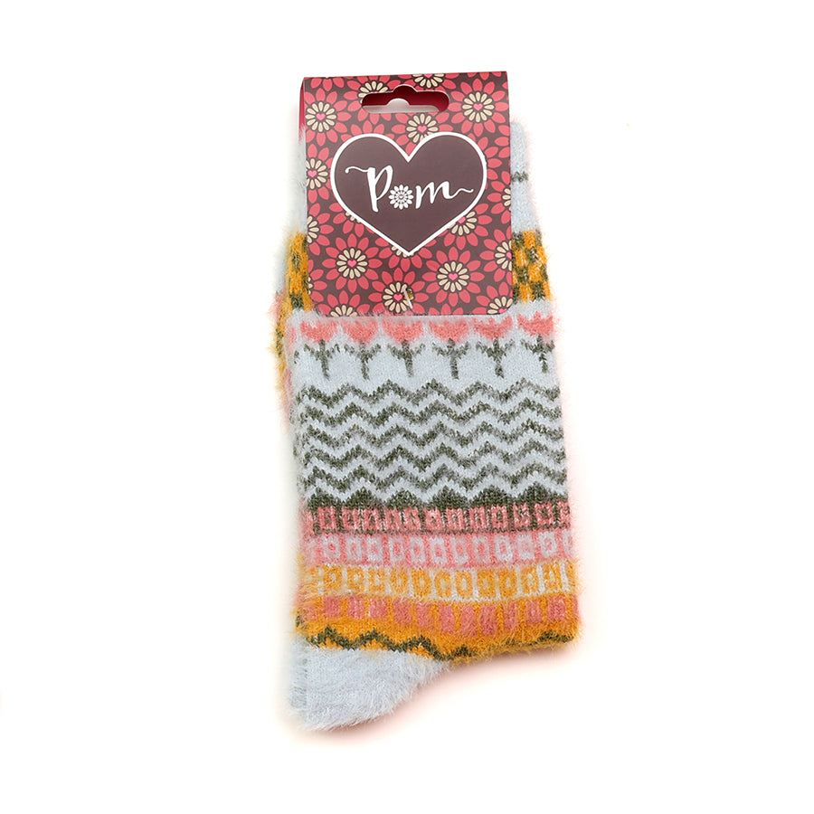 A pair of fluffy vegan socks with multicoloured and pale blue patterns are displayed, featuring a heart-shaped “Pom” label attached at the top.