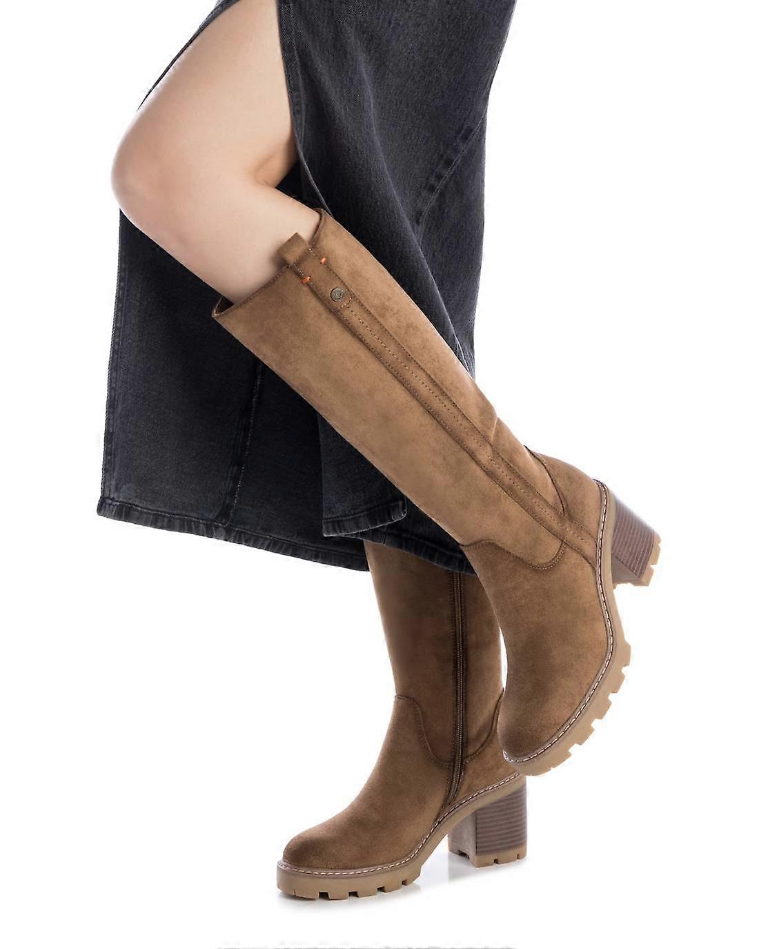 A person wearing a black skirt and taupe high-top boots with lug soles, posing against a white backdrop.