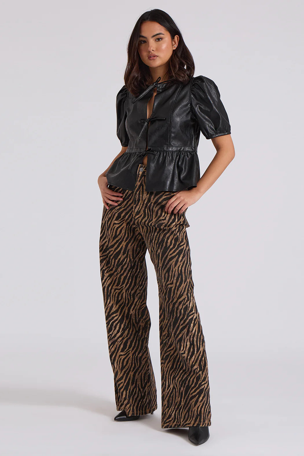 A person in a black leather top with puffed sleeves and zebra wide-leg jeans poses confidently, showcasing the bold zebra print pattern against a plain background.