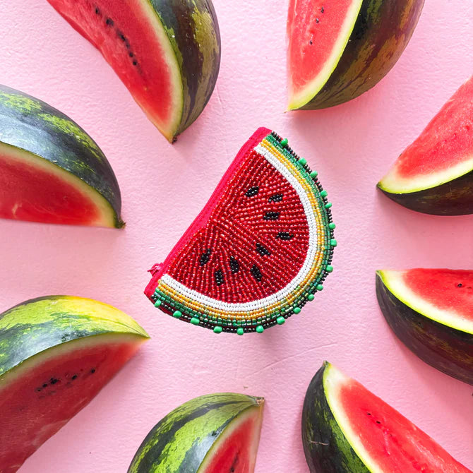A vegan-friendly accessory, this beaded Watermelon Purse—shaped like a watermelon slice—is surrounded by real watermelon wedges on a pink background, ideal for your summer style.