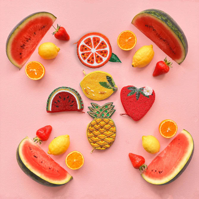 Assorted fruit-shaped coin purses, including a Watermelon Purse, displayed with real watermelons, lemons, strawberries, and orange slices on a pink background for a fresh summer style.