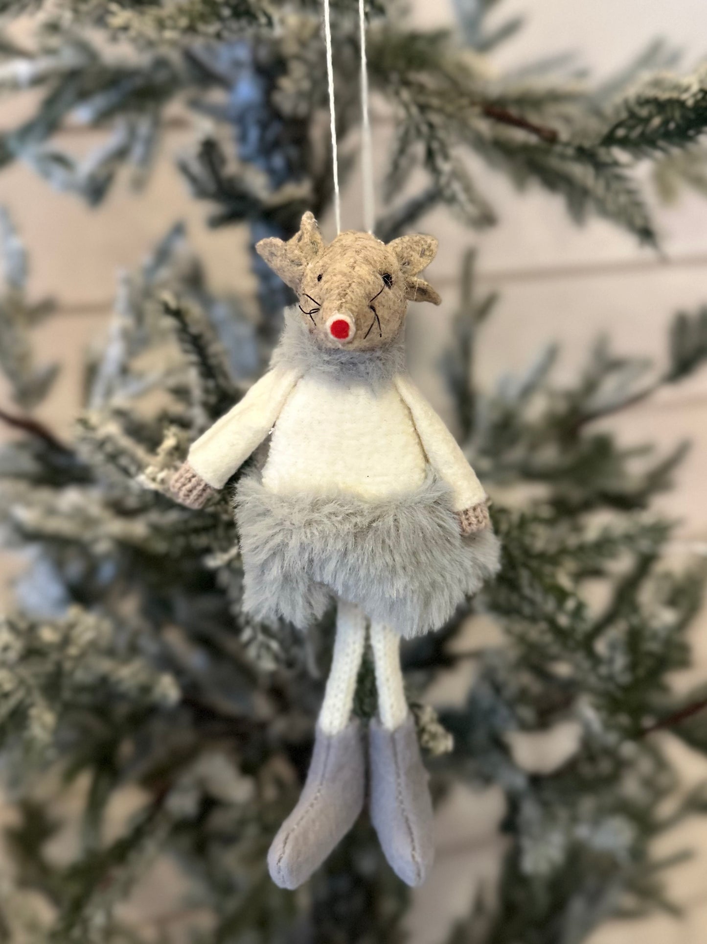 A festive decoration, this handmade reindeer with a red nose, grey boots, and a fluffy skirt hangs from a frosted Christmas tree branch—ideal for your festive décor.