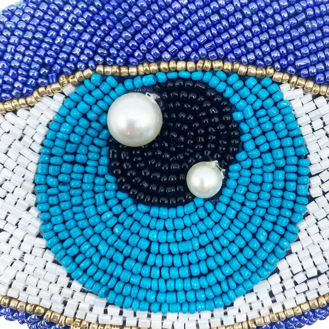 Close-up of the Glimmer Eye Purse, a vegan-friendly coin purse with a beaded eye design in blue, white, black and gold, finished with two pearl-like beads on the iris and pupil.