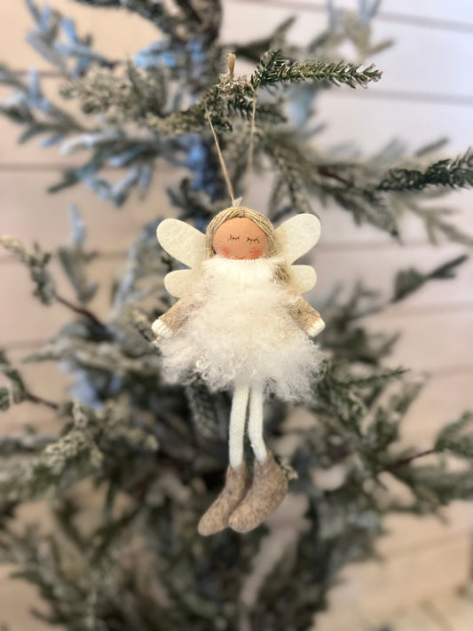 A handmade Christmas angel decoration with white wings, a fluffy white dress, and boots hangs from a frosted Christmas tree branch, adding festive cheer to your holiday décor.