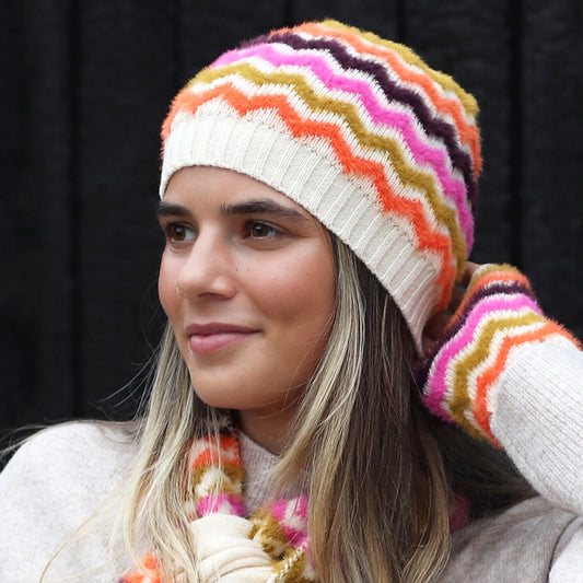 Woman in a colourful chevron beanie hat, scarf, and matching gloves, gazing to the side against a dark background—ideal for winter style.