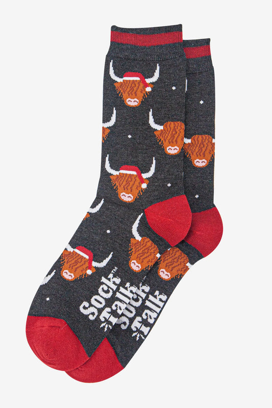 A pair of quirky men's socks—vegan-friendly Highland Cow Socks featuring red heels and toes, cartoon cows in Santa hats, and "SOCK TALK" printed on the soles.