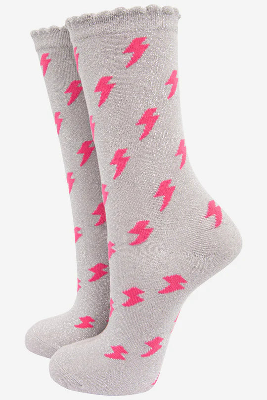 Designer womens socks with a chic twist: these grey glitter socks feature striking pink lightning bolts, elegantly displayed upright on a light-coloured background.