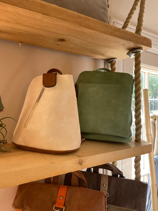 Two leather bags, including a green rucksack for the fashion-conscious individual, sit on a wooden shelf with rope supports. Another brown bag is partially visible on the lower shelf.