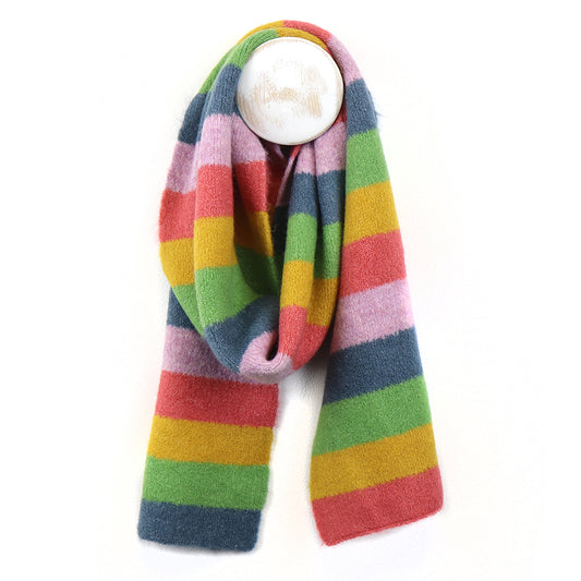 A cosy vegan scarf with wide horizontal stripes in green, blue, yellow, pink, and red hangs from a round white hook against a plain white background.