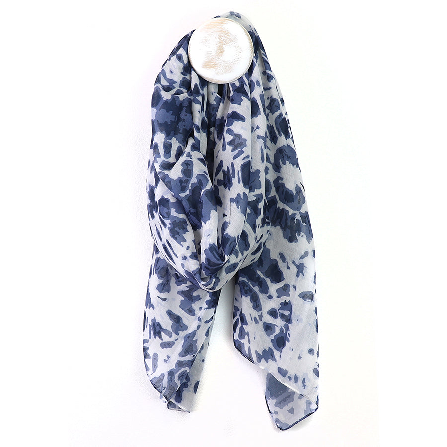 A recycled blend scarf with a blue and white pattern hangs loosely from a circular wall hook against a plain white background, combining style with an environmentally-friendly touch.