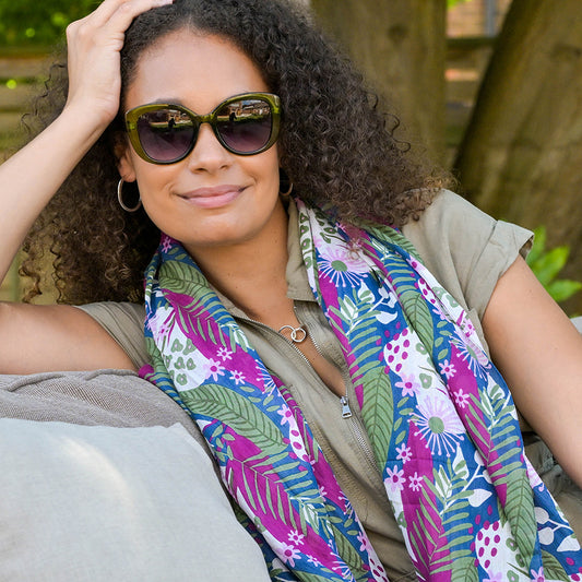 Person wearing sunglasses and a luxurious botanical print scarf, sitting outdoors on a cushion.