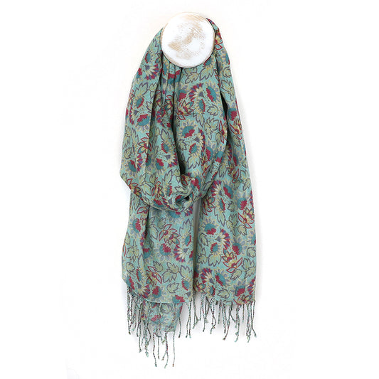 A luxurious accessory, this floral-patterned scarf with tassels hangs elegantly against a white wall, draped over a round hook.