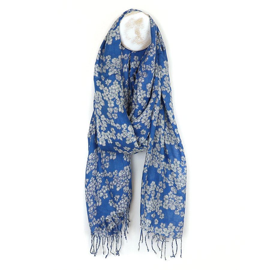 An elegant scarf with a luxurious cherry blossom print in blue and white, featuring fringed ends. Displayed against a light background, this accessory adds a touch of sophistication to any ensemble.