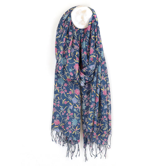 A designer scarf with pink and yellow floral patterns delicately hangs against a white background. This blue floral vine scarf, featuring fringed edges, is a fashion-forward accessory perfect for any wardrobe.
