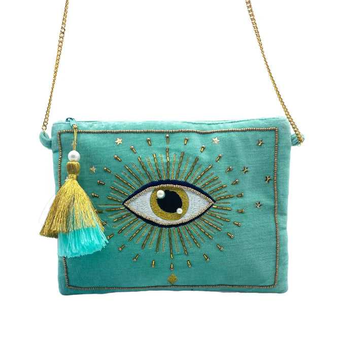 A turquoise Glimmer Crossbody Bag featuring a gold chain strap, gold and blue tassel, and an embroidered eye motif—this vegan-friendly accessory gleams with gold detailing on the front.