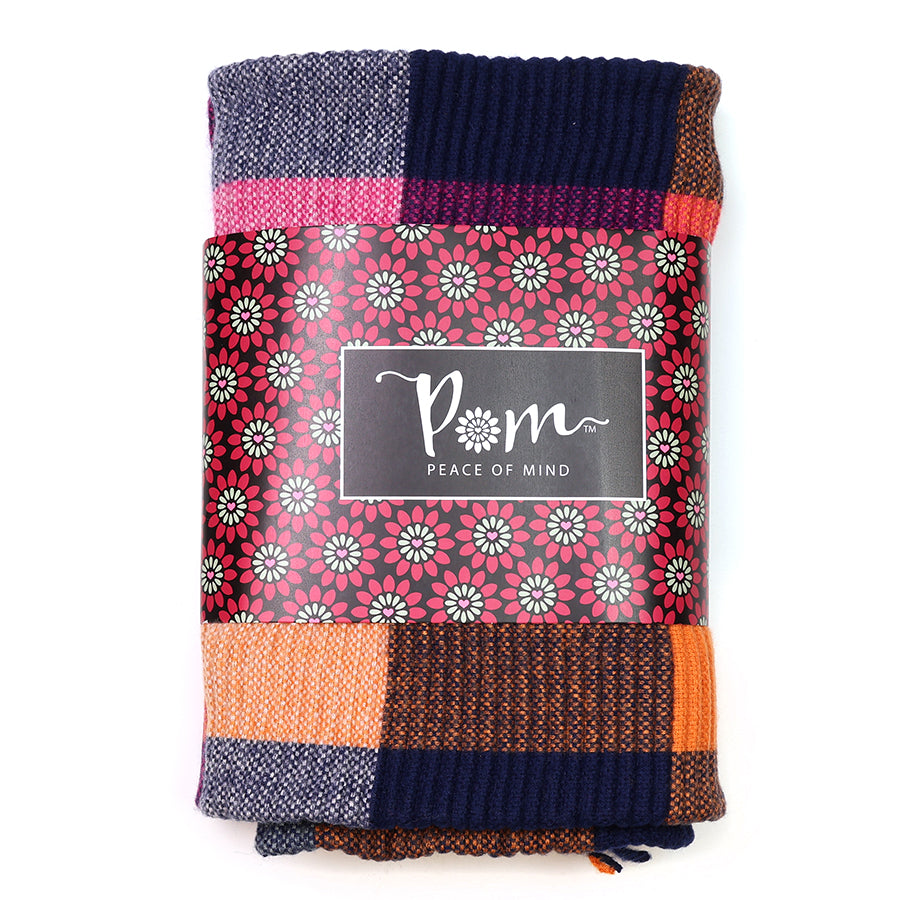 A folded multicoloured knitted blanket with a floral-patterned label bearing the words POM Peace of Mind, ideal as a stylish accessory or a cosy alternative to a rust and pink scarf.