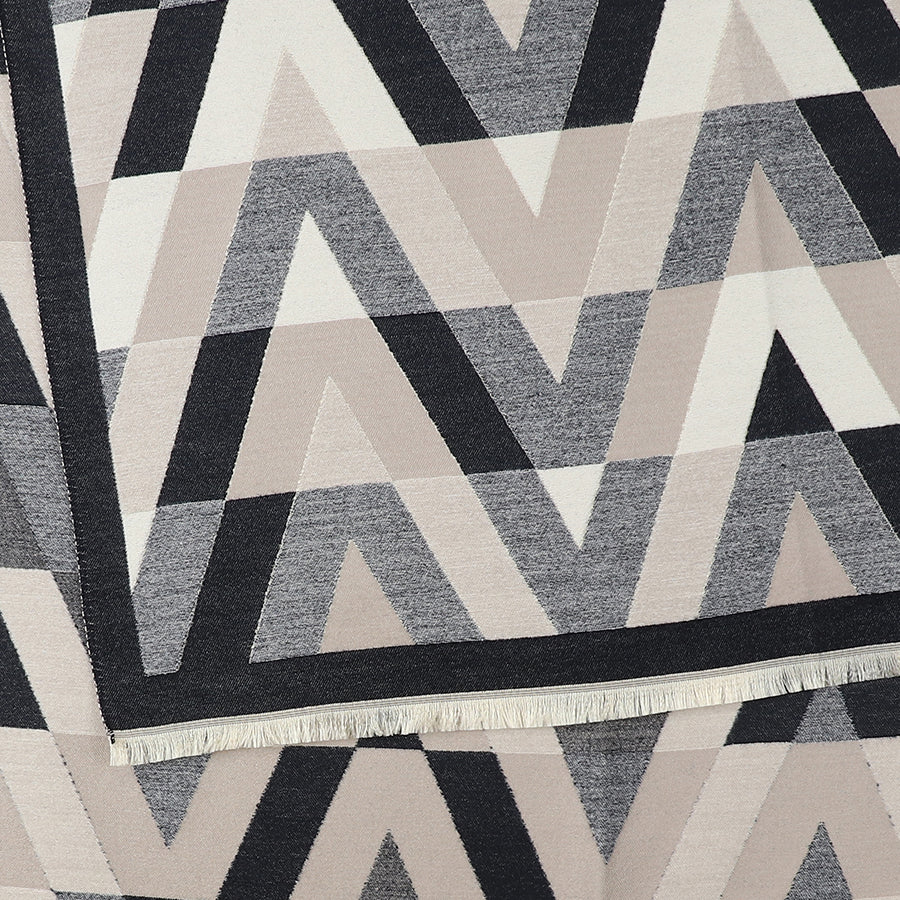 Geometric-patterned chevron scarf in tones of black, grey, and beige, displaying zigzag and triangle motifs with a visible fringe along one edge.