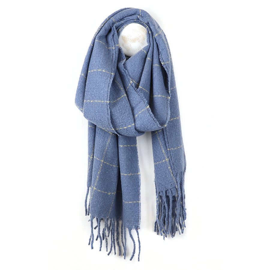 A cosy winter scarf in blue featuring a subtle check pattern and fringed ends is laid out on a white background.