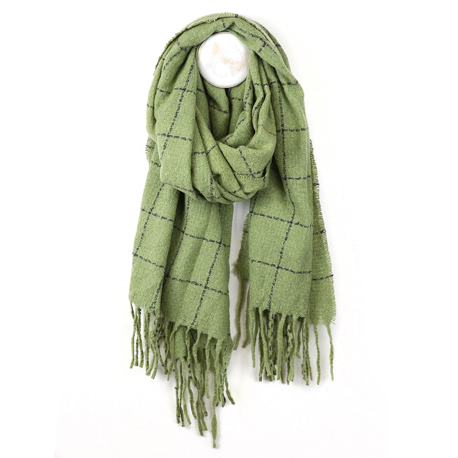 A cosy green checked scarf with a black check pattern and fringed ends, hanging from a white wall hook.