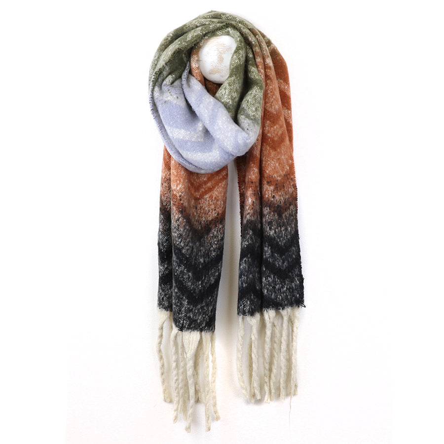 A long, fringed chevron scarf with a zigzag pattern in green, lavender, rust, black and cream colours hangs on a white hook.