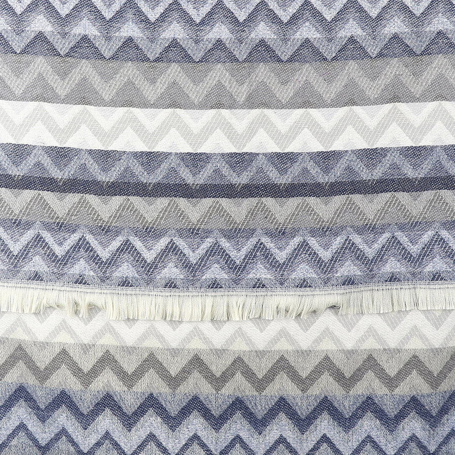 A chevron scarf woven with alternating horizontal zigzag patterns in shades of blue, grey, and white, featuring a fringe near the centre.