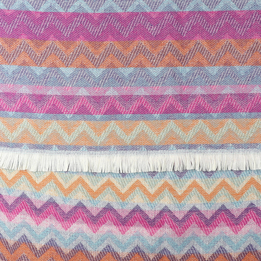 Colourful chevron scarf with zigzag patterns in purple, blue, orange and pink shades, featuring a white fringe along one edge.