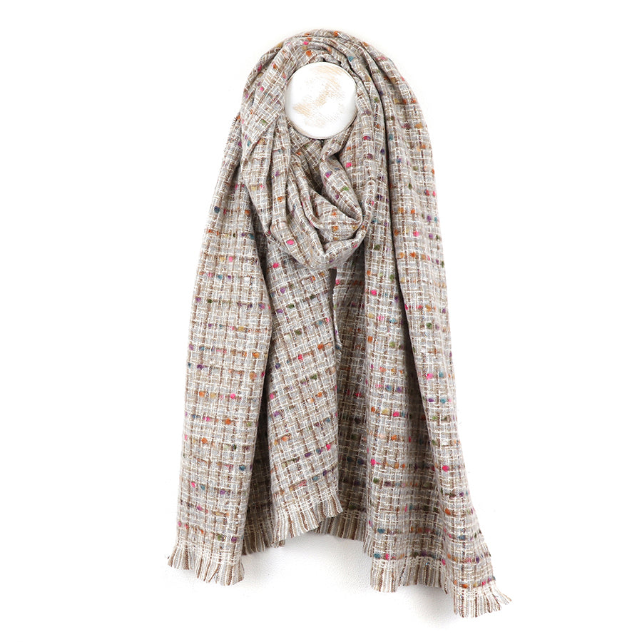A soft blend scarf in beige with a multicoloured checked pattern and fringed edges, this cosy winter accessory hangs on a hook against a white background.